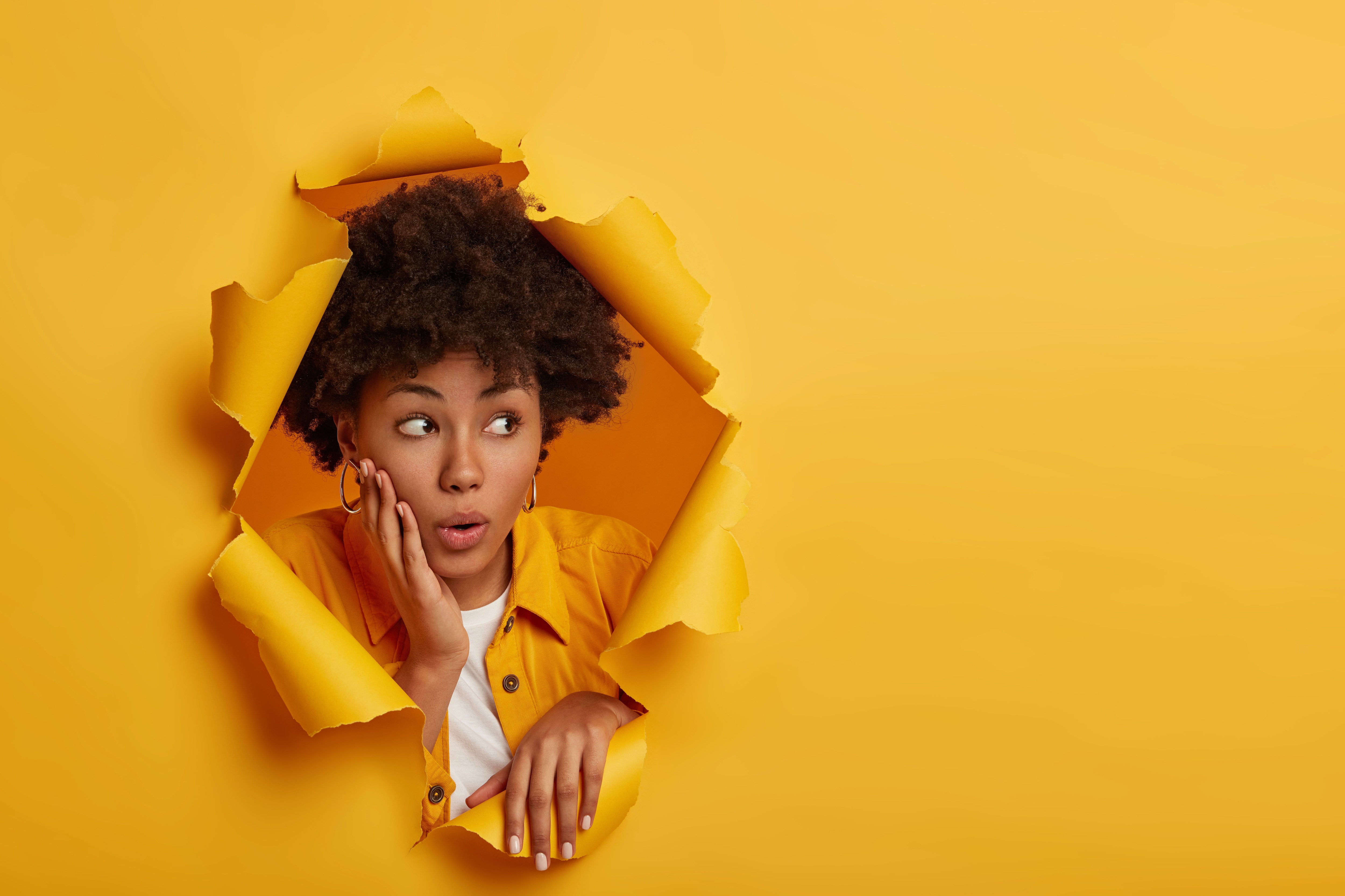 photo of a curious looking woman breaking through a wall of yellow paper