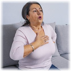 Photo of a woman seated on a couch and holding her chest