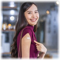 Photo of a smiling woman pointing at a small bandage on her arm