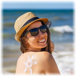 Photo of a woman at the beach with a sun down on her shoulder with sunscreen lotion