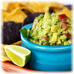 Photo of a bowl of guacamole and some chips in the background