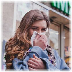 Photo of a woman blowing her nose outside while wearing multiple layers of clothing