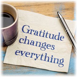 Photo of cup of coffee and pen sitting on the edges of napkin reading "Gratitude changes everything"