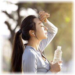 Image of a woman holding a bottle of water while resting during a run outdoors