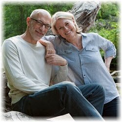 A senior couple seated on the banks of a stream in a green forest