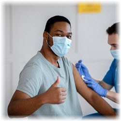 Photo of a man receiving an injection while giving a thumbs up gesture