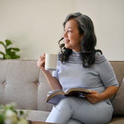 Photo of woman on couch drinking coffee and reading a book