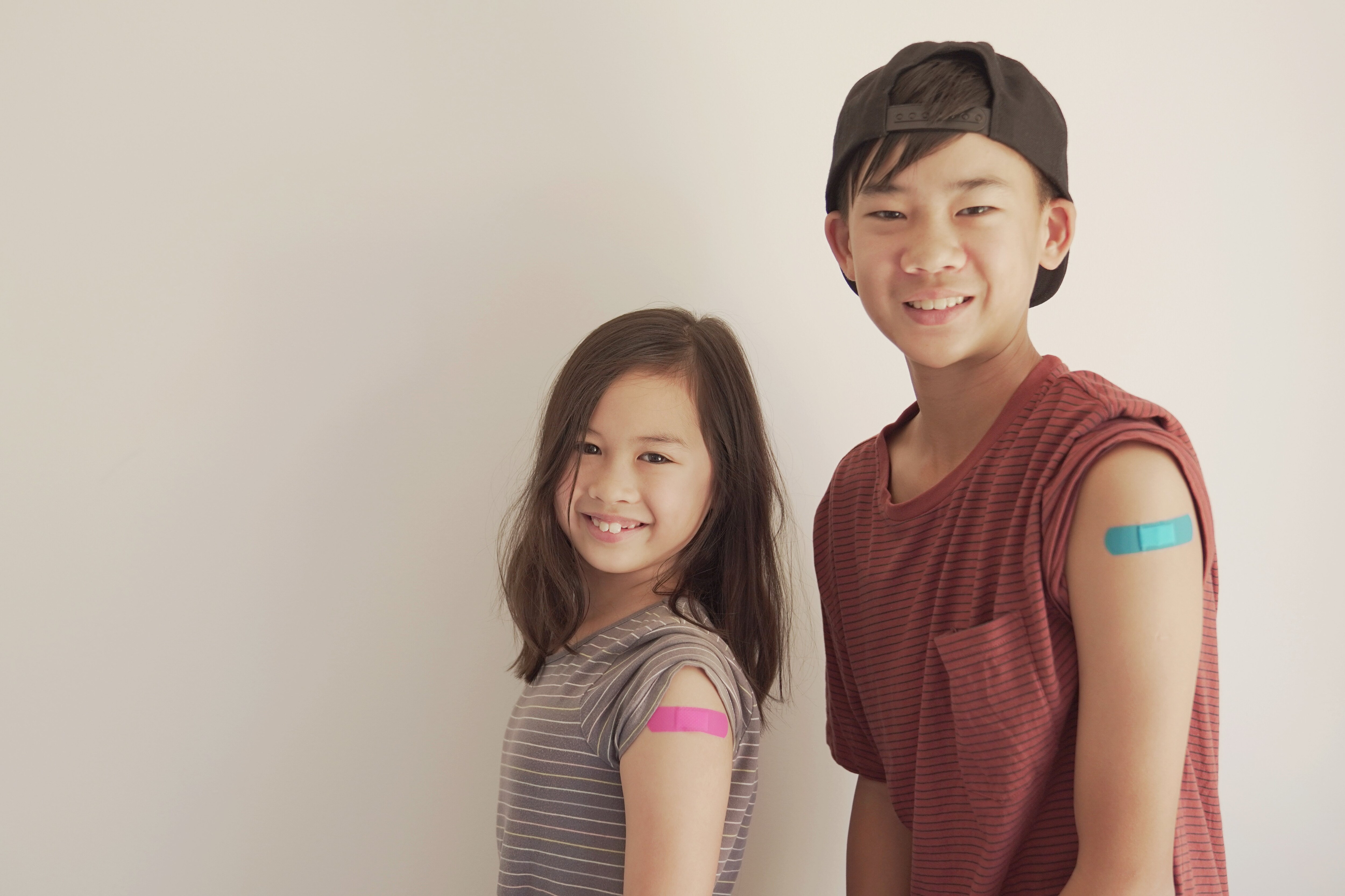 Photo of two kids who got a vaccinated have a band aid on their arm