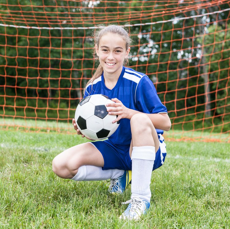 Photo of Teenage girl who plays soccer in her uniform holding a soccer ball on the soccer field