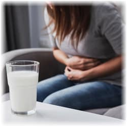 Photo of a woman sitting and holding her stomach with a glass of milk on a table in front of her