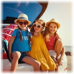 Photo of three little girls sitting on the open trunk of a hatchback vehicle at the beach